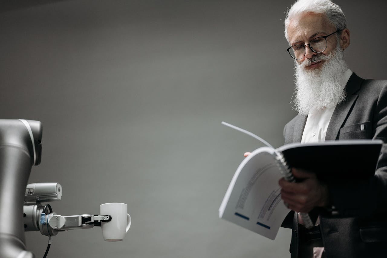 Elderly man reads as a robotic arm holds a coffee cup, showcasing technology integration.