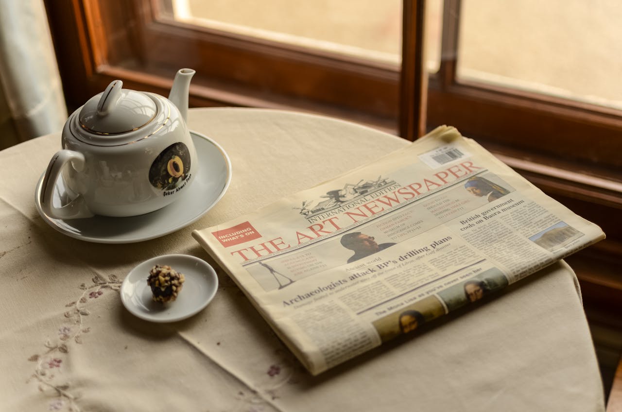A serene indoor scene with a teapot, a newspaper, and a chocolate treat by the window.